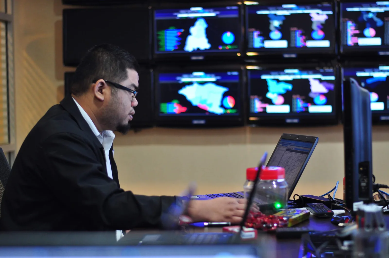 Analysts working in front of a live monitoring video wall in an operations war room